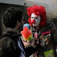 Interview d'un manifestant déguisé en clown devant un bâtiment en flammes